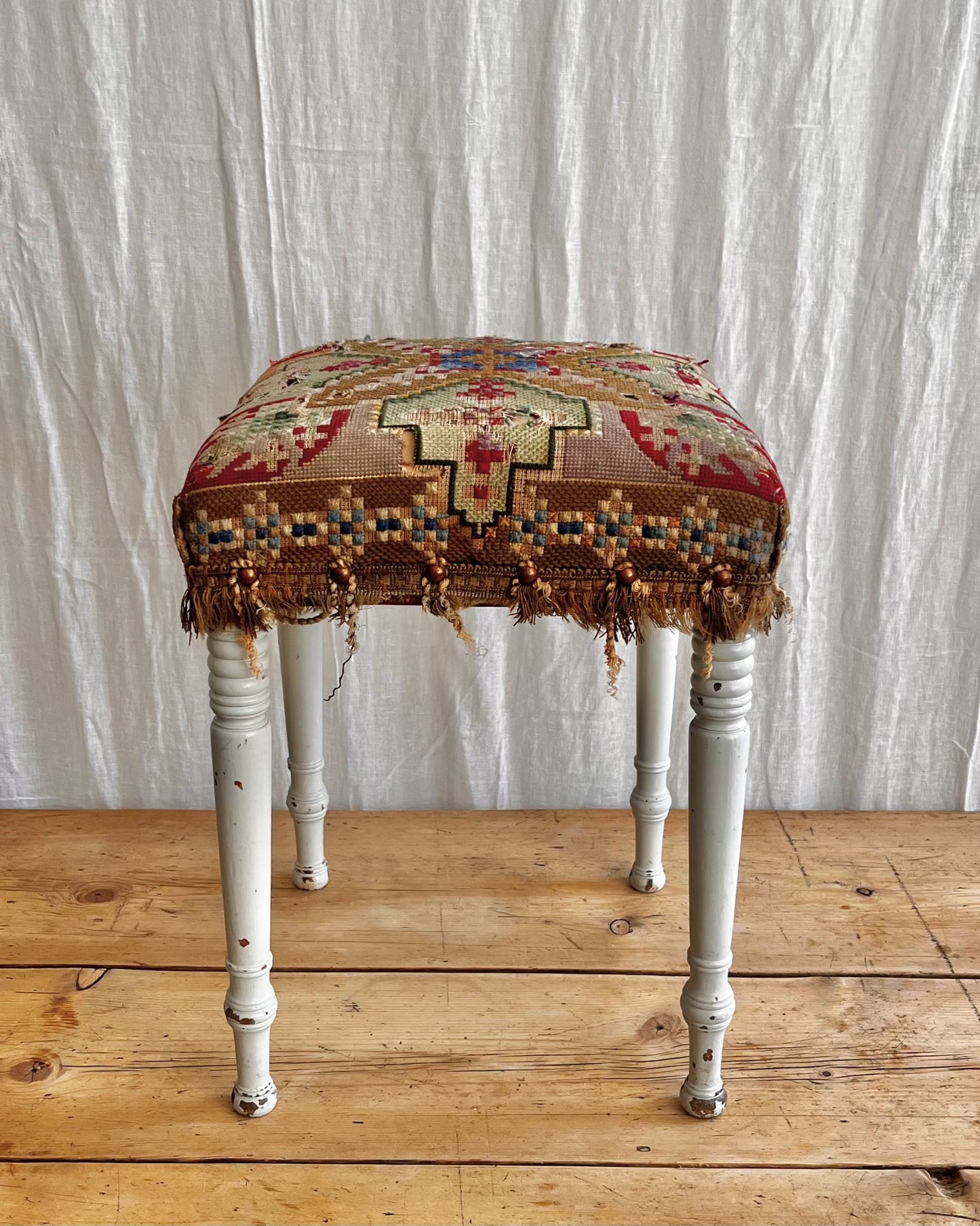 white painted antique folk art stool with a hand sewn striking tapestry seat cover